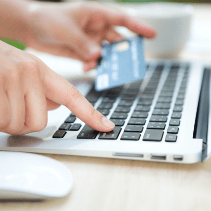 person typing on keyboard holding credit card